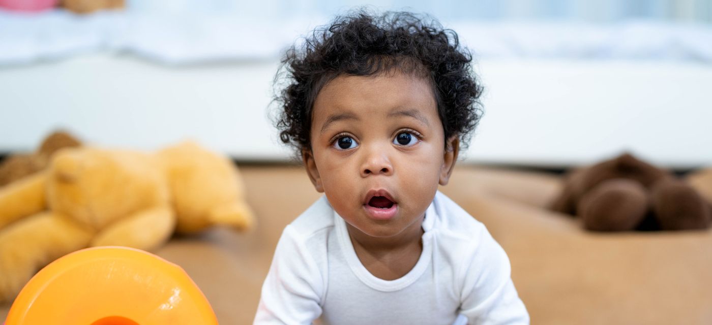 Baby with big brown eyes crawling on the floor with stuffed animals.